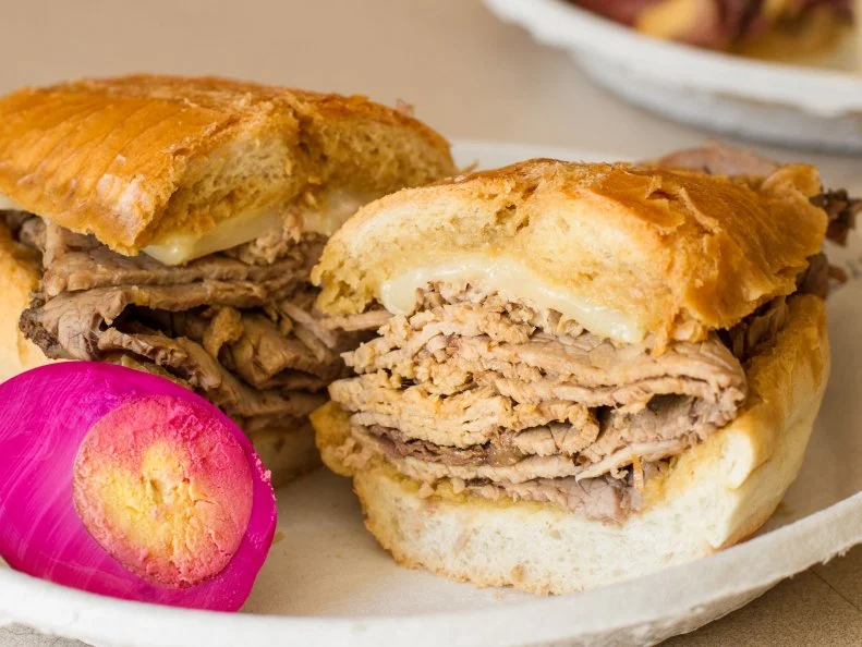 When a sandwich is so revered, it's not uncommon for a few people to lay claim to it. Such is the case with the invention of the French dip sandwich, fought over by Philippe The Original and Cole's, both in Los Angeles. However, most Angelenos believe that Philippe's story edges out Cole's, especially because Philippe's has served the iconic sandwich for nearly a century. Founded in 1908 by Philippe Mathieu, the restaurant ascribes the French dip discovery to pure accident when, in 1918, Mathieu inadvertently dropped a French roll into the roasting pan filled with beef au jus. A police officer happily gobbled down the sandwich despite the soaked bread and returned the next day with his pals, requesting the "dipped" sandwich once again. It landed on the menu helped make Philippe's a treasured culinary destination.