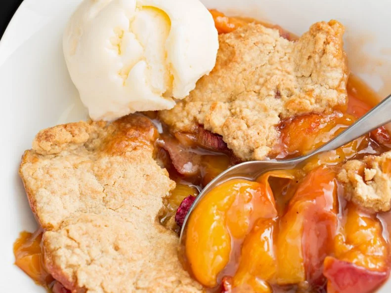 North Carolina is ninth in U.S. peach production. And when you think about it, it makes perfect sense that you’d find great Peach Cobbler at an eatery inside a farmers’ market, since that’s where the freshest food is. The State Farmers’ Market Restaurant is located on the Raleigh grounds where growers for decades have brought their crops to sell, and it’s open for breakfast and lunch. Here, the restaurant staff bustles about serving fresh-made biscuits, omelettes and sandwiches. Those alone would be enough to entice diners to stop in, but it’s even more tempting when peach cobbler is featured as the dessert of the day. It’s the perfect combination of sweet fruit, mild spices and a buttery, baked crust.