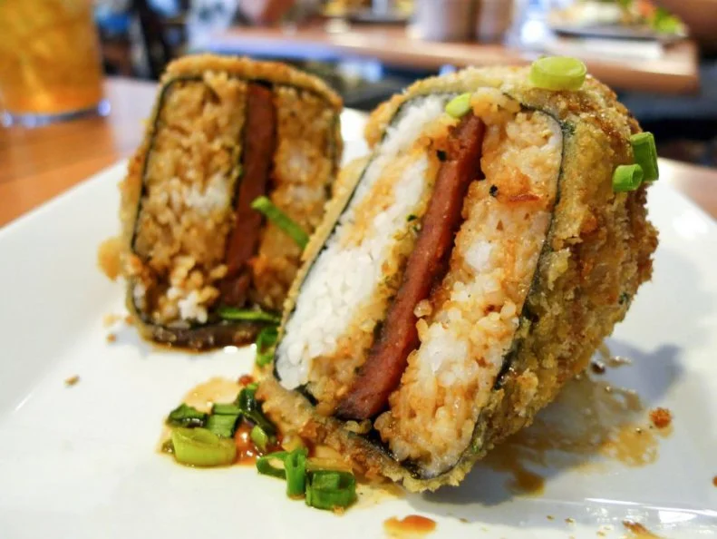 Spam may have been created on the mainland, but nowhere in the United States is it as popular or beloved as in Hawaii. The Aloha State goes through about 5 million pounds of the canned meat per year. Itâ  s the star ingredient in one of the islandâ  s most-iconic dishes, Spam musubi, which is basically sushi with Spam instead of raw fish. Typically, the dish combines the canned pork product with a square of rice, wrapped in nori (Japanese seaweed). Mauiâ  s Da Kitchen makes it sizzle. The meat-like product is breaded and deep-fried, then drizzled with sweet-soy kabayaki sauce.