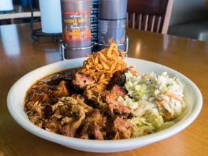 The signature dish of Burnt End BBQ restaurant, The Burnt End Bowl with Pulled Pork, rests on a table inside the restaurant, as seen on The Grill Dads, Season 1.