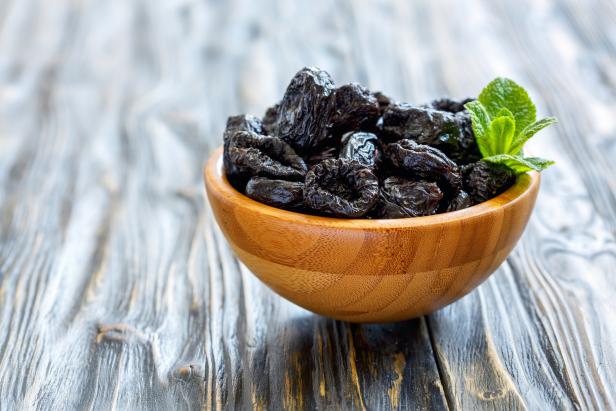 Dried black plums in a bowl on old wooden table, selective focus.