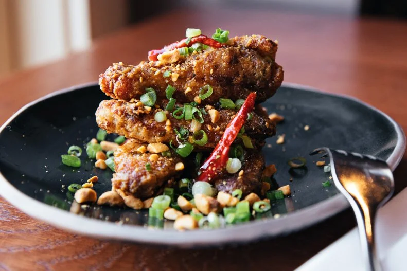 This South Carolina spot takes a little Asian inspiration for its chicken wings. Chef-Owner Kevin Johnson cures the wings overnight and then confits them in a little duck fat to make them more tender. They are then dredged in rice flour and cornstarch and fried to a crisp before being tossed in a special housemade sauce. Before serving, they are topped with spicy peanuts that have been seasoned with togarashi, scallions and dried chiles.