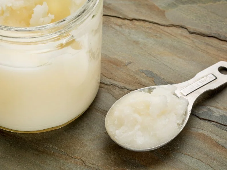 measuring tablespoon and glass jar coconut cooking oil on a slate rock background