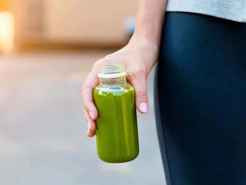 Woman drinking vegetable smoothie after fitness running workout on summer day. Fitness and healthy lifestyle concept