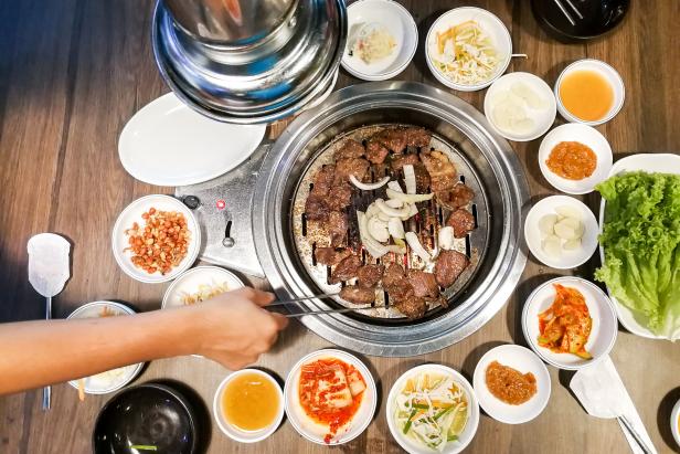 Person barbecue beef on bbq pit during korean meal set in restaurant