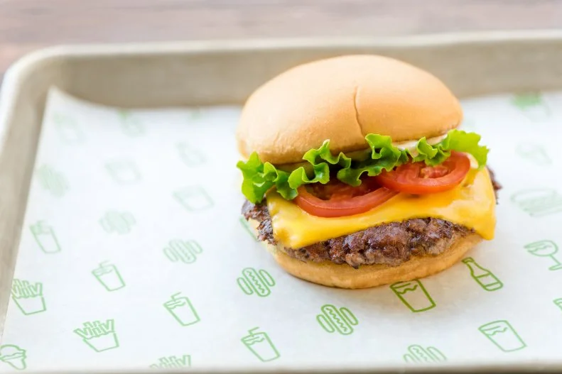 Danny Meyer's "modern-day roadside burger stand" started serving burgers, hot dogs, fries and milkshakes from an open-air snack bar in NYC's Madison Square Park back in 2001. Its ShackBurgers have become so coveted that the chain now has locations dotting the country from coast to coast and popping up as far away as Japan, Bahrain, Turkey and the U.K. What's made Shake Shack's burgers such an international sensation? Their simplicity. The proprietary blend of 100 percent Angus beef is freshly ground, formed into thin patties and cooked to medium doneness. Then it's covered with a slice of American cheese, lettuce, tomato and ShackSauce and tucked into a Martin's Potato Roll.