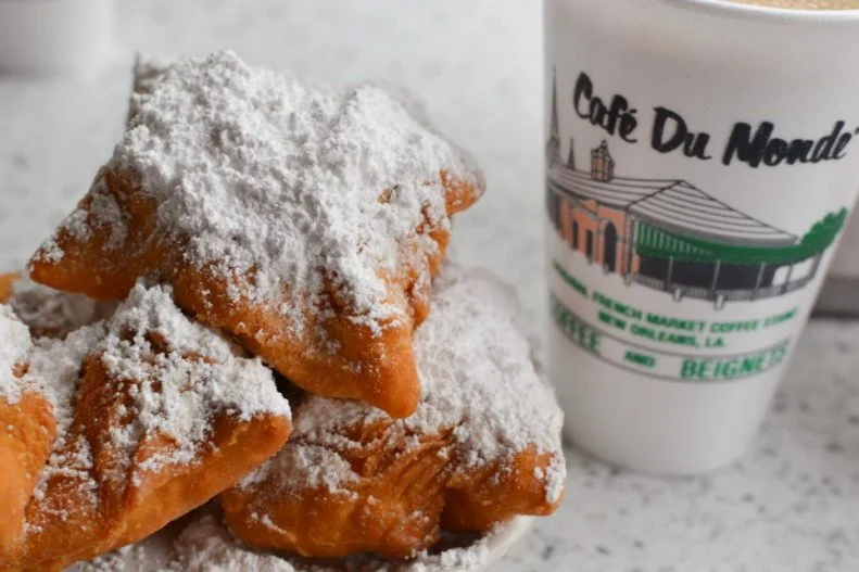 Ordering up a powdered sugar-dusted stack of beignets â   specifically at the original CafÃ© du Monde, in the French Market â   invariably makes every New Orleans visitor's must-eat bucket list. Brought to Louisiana by the Acadians (French-speaking Canadians, who came to be later known as Cajuns), the fried squares of choux dough are best served piping hot, next to a bracing cup of chicory-laced coffee.