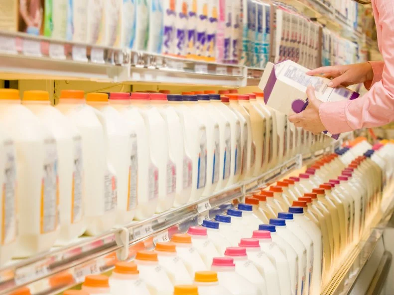 Woman checking ingredients on back of milk carton in supermarket