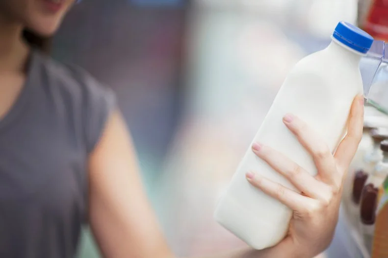 Woman checking label on milk in supermarket dairy section