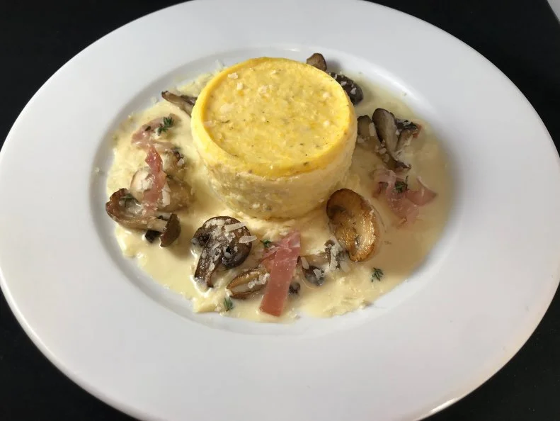 In the South, grits — or coarsely ground corn meal — serve as the foundation for many down-home dishes, whether boiled and served as breakfast porridge, combined with shrimp for a low-country entrée or folded with cheese for a potluck. At his fine dining restaurant, Highlands Bar & Grill, Birmingham chef Frank Stitt elevates grits from humble pantry staple to a sophisticated soufflé-like appetizer. A menu mainstay since day one, the Baked Grits feature locally milled organic, coarse yellow grits from Coosa Valley which are boiled and combined with butter, white pepper and finely grated Parmesan for savory depth. Portions are baked in buttered ramekins in a hot water bath to achieve their airy texture, plated with a wild mushroom-sherry-vinegar sauce, smoky Benton’s country ham, thyme and more freshly grated Parmesan.
