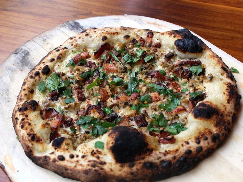 Boston-style pizza — it’s a thing. Get a taste at Area Four, where Chef-Owner Jeff Pond borrows from both New Haven and Neapolitan pizza-making traditions to create his signature A4 pies. Tender dough and crisp crusts serve as the base for a slew of seasonal, locally-inspired toppings. For a taste of New England, opt for the Wellfleet Clam & Bacon. Pond starts with his hand-stretched dough, which he makes with a 16-year-old sourdough starter and ferments for up to 30 hours. Once the dough is ready, he slathers on a clam sauce seasoned with hot peppers and parsley, then heaps on meaty Wellfleet cherry stone clams from Cape Cod and hefty slabs of thick-cut bacon. A final flurry of Pecorino cheese adds a tangy, salty bite that perfectly complements the clams’ brininess. Pond bakes the pizza in a wood-fired oven at 750 degrees to ensure a beautifully charred crust and kiss of smoky flavor.