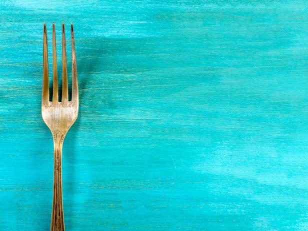 An overhead photo of a vintage fork on a vibrant turquoise wooden background texture. A restaurant menu or special offer banner design template