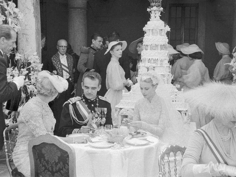 (Original Caption) Prince Rainier III, ruler of Monaco, and his lovely American princess-bride Grace Patricia Kelly are shown in the palace during the reception which followed their marriage this morning before the high altar of Monaco cathedral at a nuptial mass. In background in the huge multi-tiered wedding cake. Monsignor Paolo Marella, papal nuncio to Paris read a special message from Pope Pius XII to the prince and princess.
