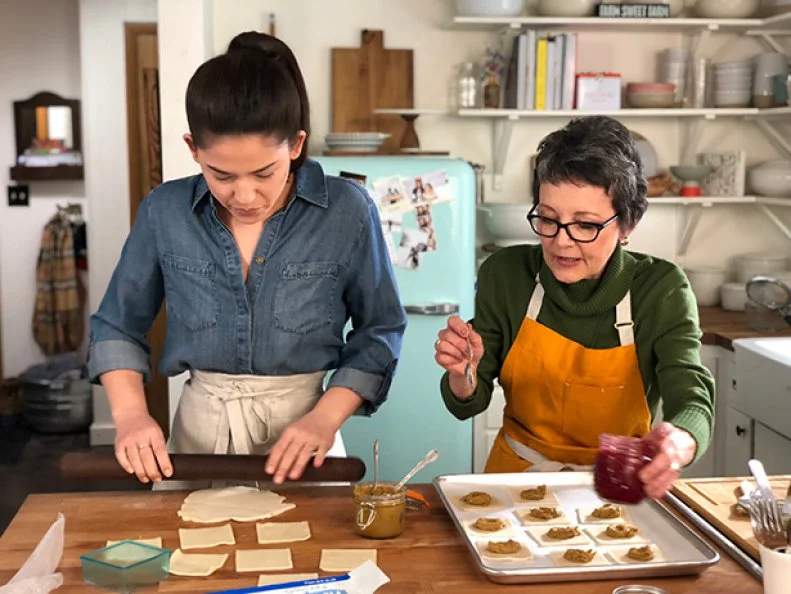 Molly rolls out pastry dough while Roxanne places pistachio butter on cut pastries