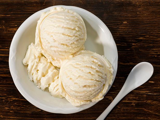 Vanilla ice cream in a bowl with a spoon on a wooden board