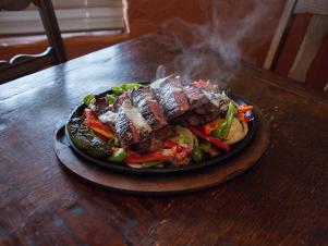 Fajitas served on a sizzling platter topped with peppers, onions and jalapeños at Ninfa's, as seen on Comfort Food Tour, Season 2.