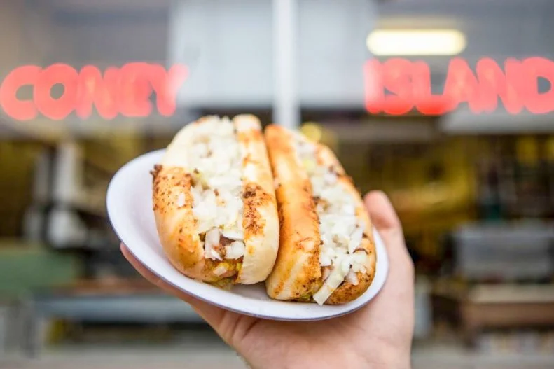 A short drive from the Michigan and Ohio borders, Fort Wayneâ  s Famous Coney Island picks up where celebrated Coney traditions of Detroit and Cincinnati (sort of) stop. Owned and operated by the same family for more than a century, this lively eatery has worked its way into the cityâ  s culinary fabric. It sells around a million hot dogs per year. Why the fuss? Its legendary dogs are just that good. Each frank is grilled and placed inside a steamed bun with mustard, hand-chopped onions and homemade Coney sauce thatâ  s essentially Greek bolognese. The must-order is â  three and a bottle,â   three dogs with all the fixings and a bottle of Coke.
