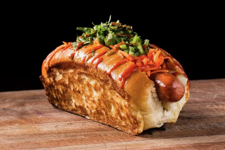 The simple hot dog gets a complete makeover at this Alexandria place. All-beef franks are made with natural casings from grass-fed cows reared with no antibiotics or hormones, placed within toasted split-top New England-style buns made fresh and delivered daily by Ottenbergâ  s Bakery in nearby Washington, D.C. The most popular haute dog is the bÃ¡nh mÃ¬ dog, a rainbow of flavors and textures that strikingly impersonates the original sandwich with sliced jalapenos, matchsticks carrots and cucumber, fresh cilantro and hearty, twisty squeeze of sriracha mayo. Those fresh and vibrant flavors liven up the savory and snappy griddled frank and the toasty, butter-slathered bun.