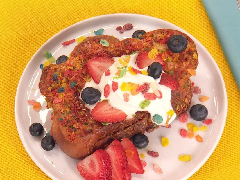 Host Brandi Molly makes a French Toast made with Challah bread which Is sliced thicker for french toast. Fruity pepples cereal In a bag that is crushed up a little with a roller, filling for inside of bread is made with cream cheese, chopped strawberries, and berries. Stuart prepares the egg batter which french toast is dipped into a final step before cooked, half and half is used giving a richer texture, little vanilla, cinammon and eggs mixed together. Bread is left thick so you can cut open to add filling without bread falling apart, dipped in egg batter then in fruity pepples cereal also, and cooked in   a pan with just butter for a few seconds finished in the oven. Toped with syrup, fresh whipped cream, berries, and a little more crunch, ready to enjoy, as seen on Food Network's Lets Eat, Season 1. 