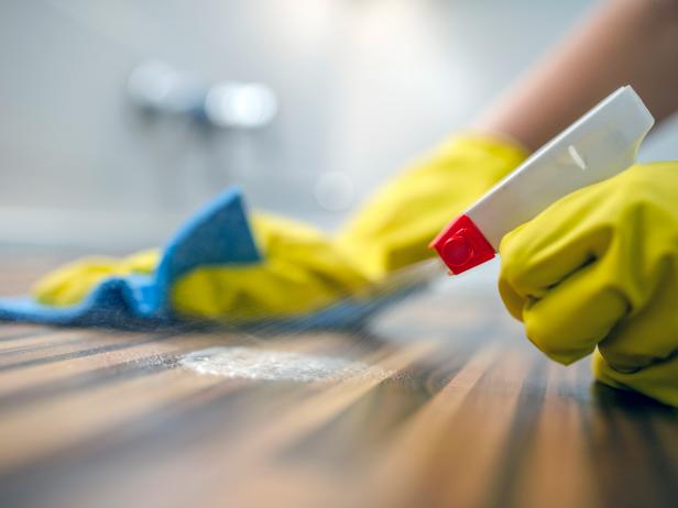 Photo of Woman or man cleaning kitchen cabinets with sponge and spray cleaner. Female or male hands Using Spray Cleaner On Wooden Surface. Maid wiping dust while cleaning her house wearing yellow protective gloves, close-up