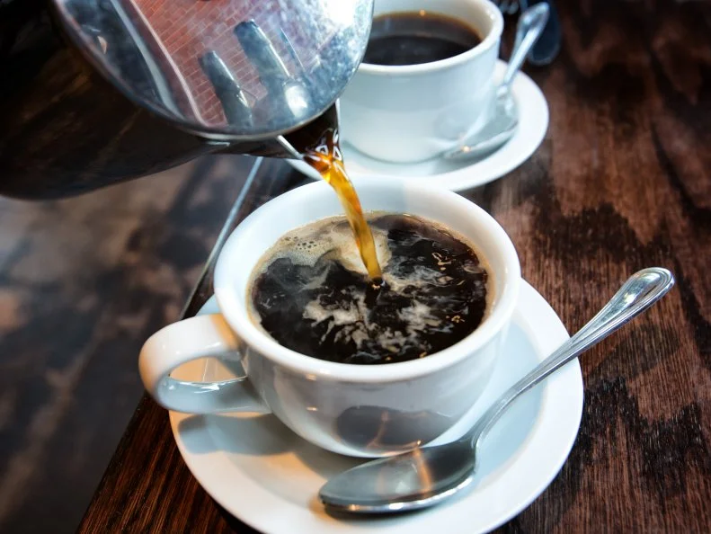 Fresh hot coffee being poured into a cup from a stainless steel french press in a trendy cafe