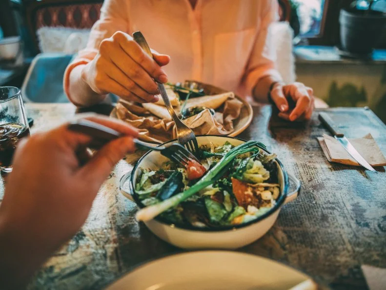 Woman taking some of her boyfriend's salad on lunch at a restaurant.