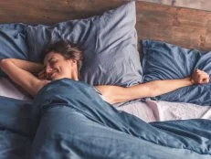 Beautiful young woman is stretching and smiling while lying in bed in the morning
