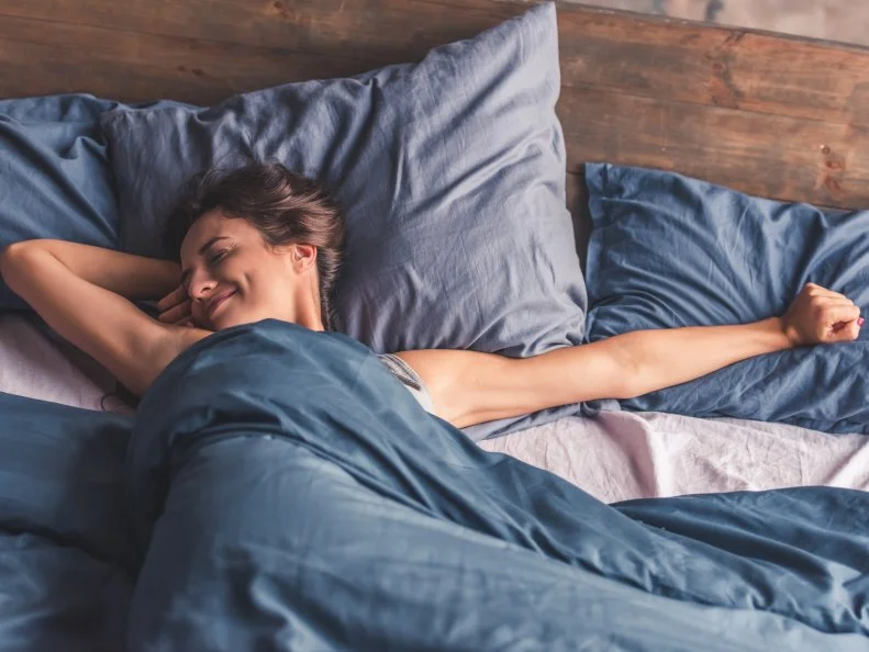 Beautiful young woman is stretching and smiling while lying in bed in the morning
