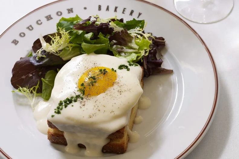 The croque monsieur is the fancy French cousin to the American ham and cheese â   an elevated combination of boiled ham between slices of sweet pain de mie, topped with grated cheese, baked, fried or grilled, then covered with decadent Bechamel sauce. Put an egg on top and it becomes a croque madame. Thomas Keller offers his own chef-y take on the latter at his renowned Bouchon Bakery in Napa. There, the internationally acclaimed chef accents thinly sliced Madrange Jambon de Paris with thick-sliced Brioche (baked on site of course), Swiss cheese and nutmeg-, clove-, pepper- and ComtÃ©-infused Mornay sauce, making the already indulgent dish even more extravagant. Take that, France.