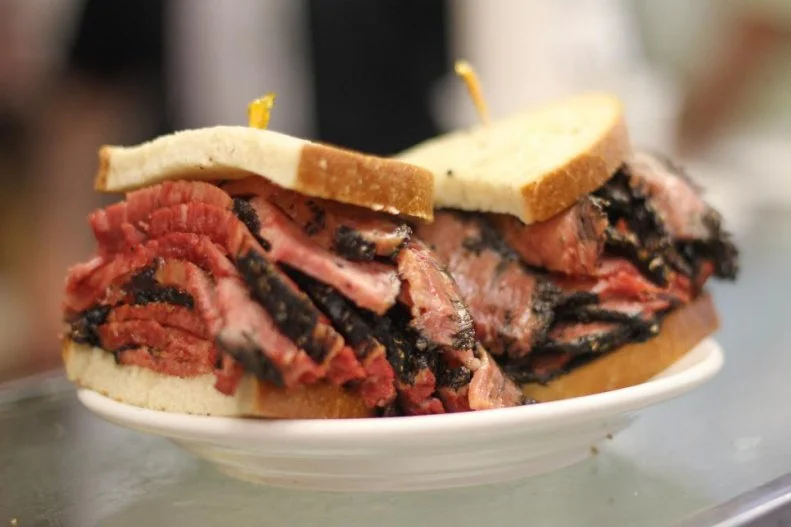 In the late 1800s, when Eastern European immigrants were arriving en mass, pastrami made its way to New York City, working its way into the Big Appleâ  s â   and Americaâ  s â   essential culinary canon. Salt- and spice-cured beef is smoked and steamed until tender, then hand-sliced â   the requirement at a proper deli â   and sandwiched in lightly seeded rye bread slathered with spicy brown mayo. Thatâ  s exactly how youâ  ll find it at Katzâ  s Deli on Manhattanâ  s Lower East Side. Since 1888, locals have rushed the counters through seemingly disorganized crowds at the cash-only cafeteria-style joint, famously pictured in films like When Harry Met Sally, for its meaty, overstuffed hot pastrami sandwiches.