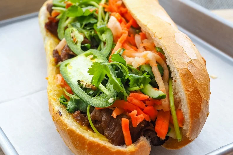 A fusion masterpiece since long before the term fusion implied culinary trends, the banh mi combines French baguettes and pÃ¢tÃ©s with Vietnamese flavors and ingredients. The result, is one of the best sandwiches ever created. Luâ  s Sandwich in Minneapolis serves one of the top takes in the U.S. Crisp, airy baguette is baked fresh daily, filled up choice of eight different proteins and traditional cilantro, cucumber, pickled carrots, daikon, jalapenos, green onions, homemade butter and pork pÃ¢tÃ©. You can go wrong with any of the picks, but the Vietnamese-style grilled pork might just be the best thing youâ  ll ever eat.