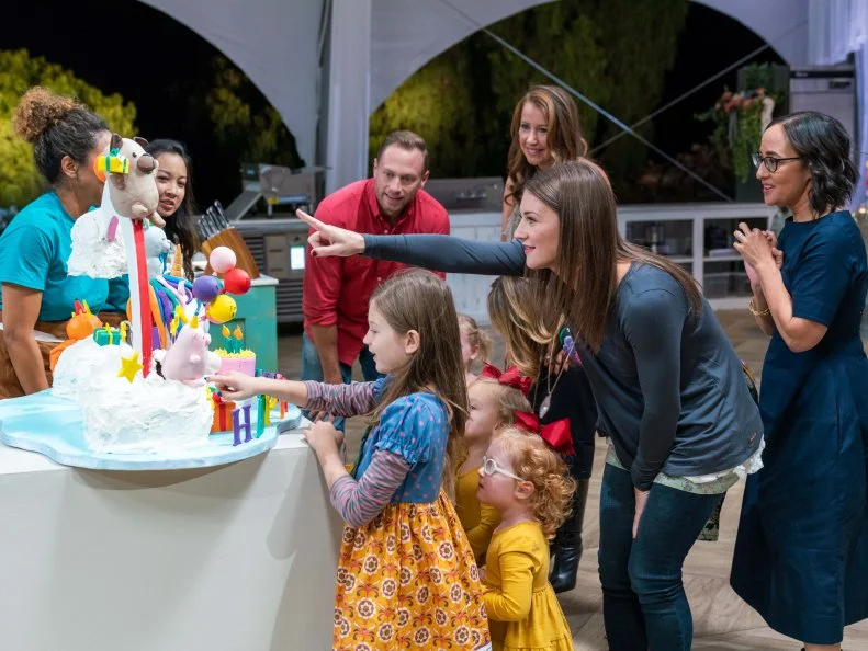 Host Giada De Laurentiis and judges Kimberly Bailey and Valerie Gordon with the clients, the Busby, parents Adam and Danielle, oldest daughter Blake and featuring the Busby Quintuplets, Ava, Olivia, Hazel, Riley, and Parker Kate, and winning competitors Kyong Bell and Dien Thach, during the cake challenge, as seen on Winner Cake All, Season 1.