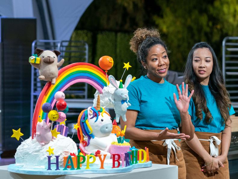 Competitors Kyong Bell and Dien Thach present their cake to host Giada De Laurentiis, judges Kimberly Bailey and Valerie Gordon, and clients, Adam and Danielle Busby, during the judging of the cake challenge, as seen on Winner Cake All, Season 1.