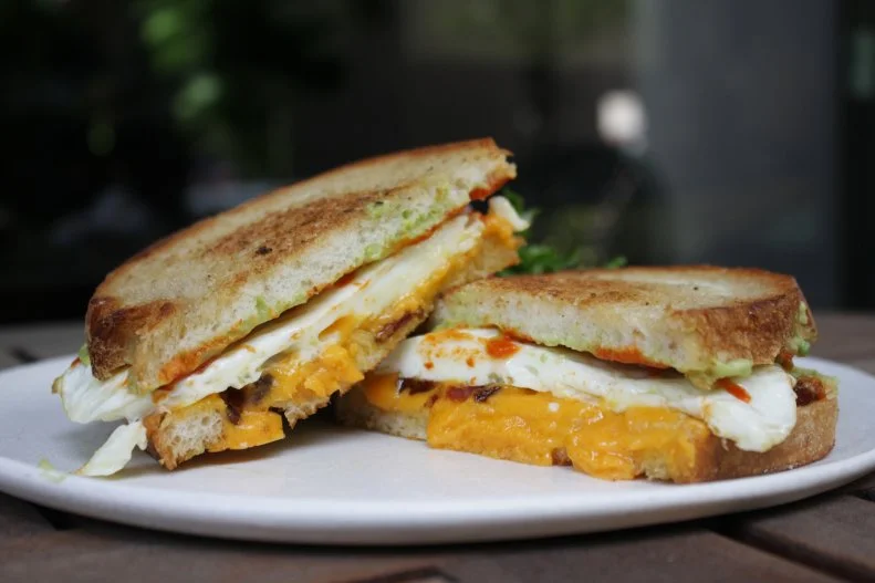 This indulgent breakfast sandwich combines all the best elements of a morning bite – it's savory, smoky and a little spicy. It starts with sourdough bread that's coated with Sriracha, then schmeared with a creamy avocado spread made with a hint of lime and creme fraiche, and topped with pork belly cured and smoked in-house, Hook's 5-year cheddar and a fried egg.