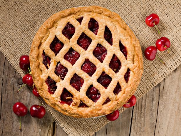 An overhead extreme close up shot of a freely baked whole cherry pie and several fresh cherries sitting on an old weathered wood  table.PLEASE CLICK HERE FOR MORE DELICIOUS PIES