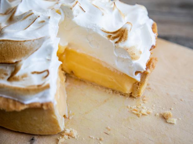 A view of a lemon meringue pie with a piece missing to reveal the delicious inside.
