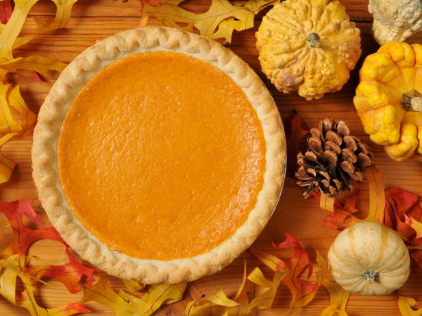 A whole sweet potato pie on an artistic set with autumn leaves, squash and gourds.