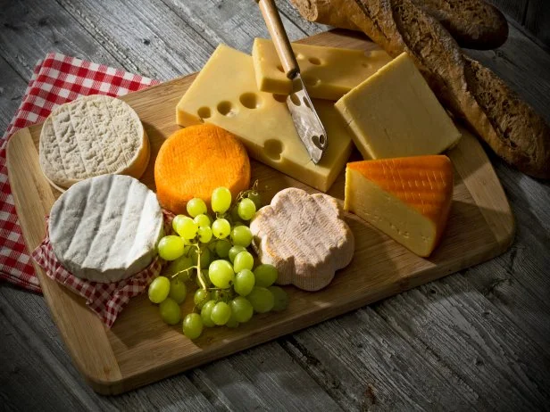 verschiedene Käsesorten (Cheddar, franz. Weichkäse, franz. Schafkäse, Camenbert aus der Normandie, Emmentaler laktosefrei, Österr. Bergkäse) und Weintrauben auf einem Holzbrett, Studio