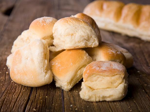 A pile of dinner rolls on a rustic wooden counter.