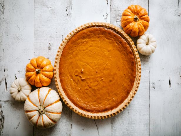 A high angle view looking down on a freshly baked pumpkin pie, just in time for your autumn or Thanksgiving season celebration.  Small decorative gourds decorate the scene.  Horizontal image with copy space.