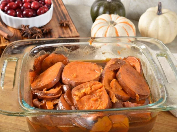Homemade candied yams in a baking dish cooling on a cutting board`