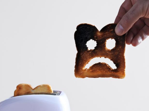 Hand holds one slices of burnt toast bread with sad face against a toaster. Sadness concept. copy space