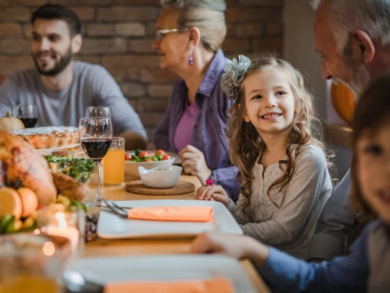 Happy little girl enjoying in conversation with her grandfather during Thanksgiving dinner in dining room.