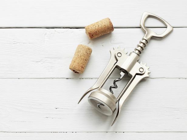 Metal corkscrew for wine and cork on white wooden background. Copyspsce.
