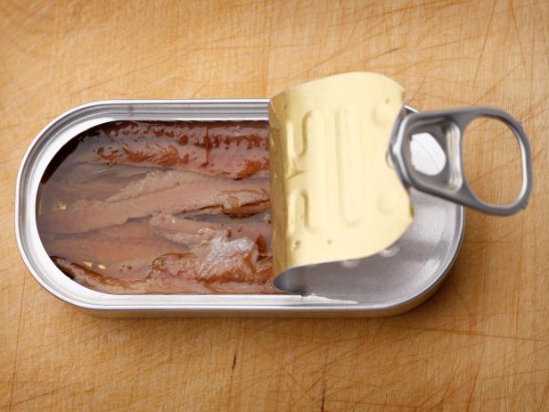 A can of anchovies in olive oil on a well-used cutting board background.