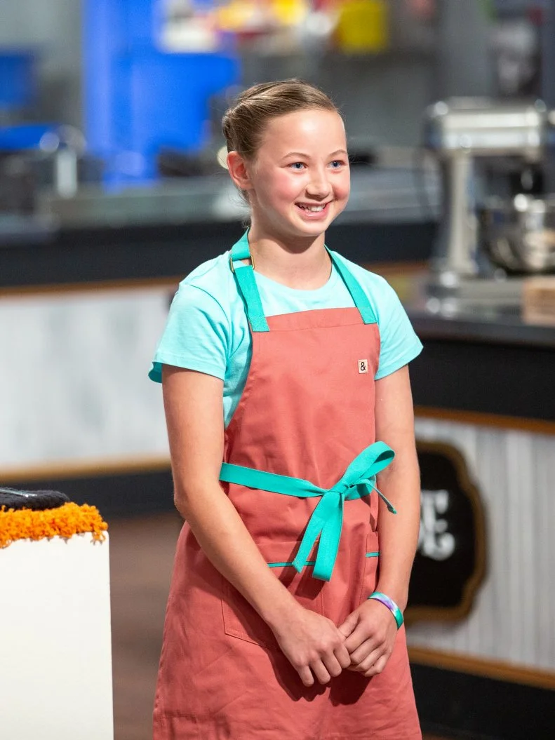 Elise standing in front of judges table, as seen on Kids Baking Championship, Season 8.