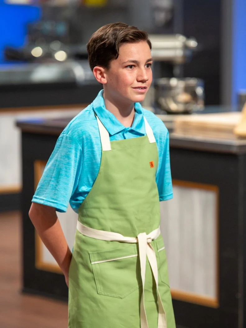 Liam standing in front of judges table, as seen on Kids Baking Championship, Season 8.