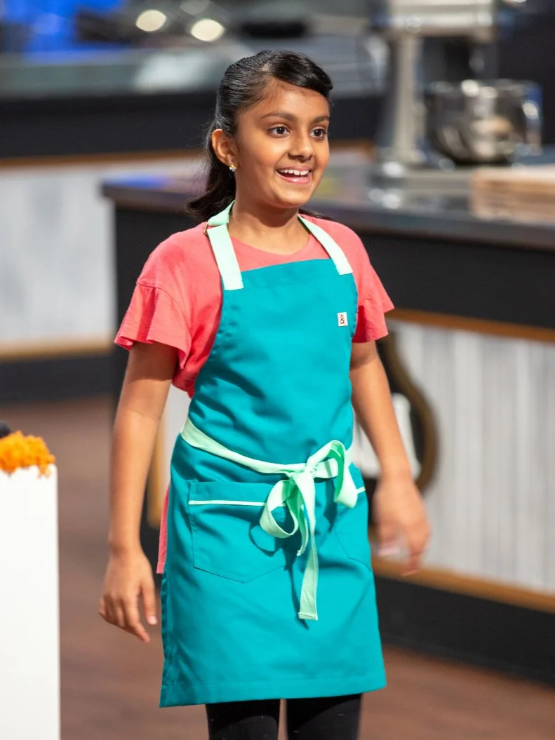 Sahana standing in front of judges table, as seen on Kids Baking Championship, Season 8.