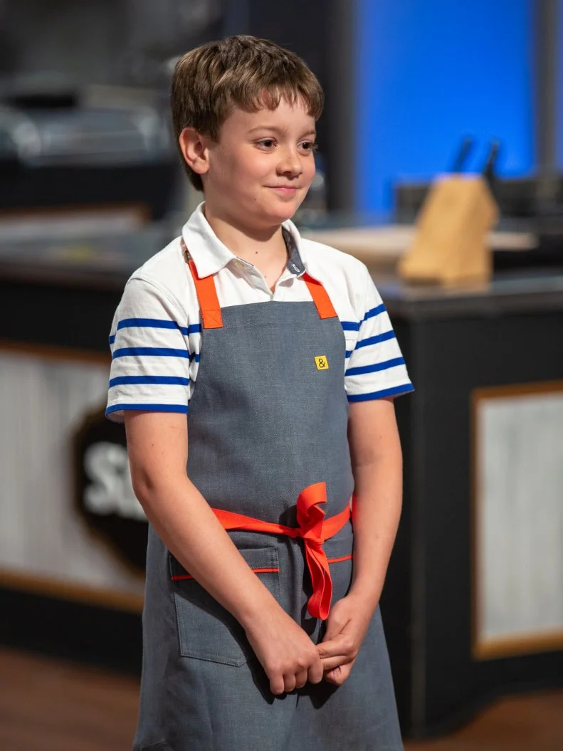 Sam standing in front of judges table, as seen on Kids Baking Championship, Season 8.