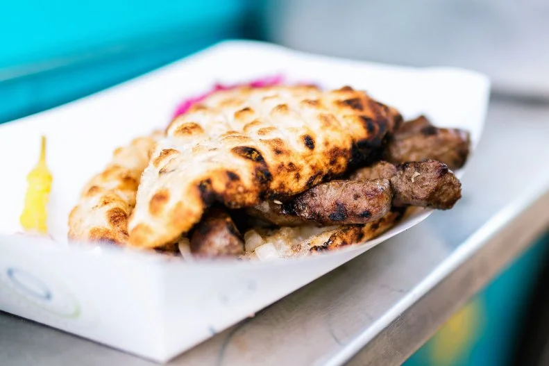 Across the Balkans, chefs and home cooks combine minced meat and garlic into thin, finger-shaped kebabs and grill them over an open flame. This sausage-like specialty can be found plain without any accoutrements, but more often than not it’s served in pillowy flatbread with flavorful condiments. That’s what you’ll find at St. Louis Bosnian food specialist Balkan Treat Box. The former food truck, now a brick-and-mortar restaurant, serves longer, denser Sarajevo-style cevapi in its homemade wood-fired pita (called somun) with raw onion and kajmak, a creamy white sauce that somewhat resembles clotted cream.